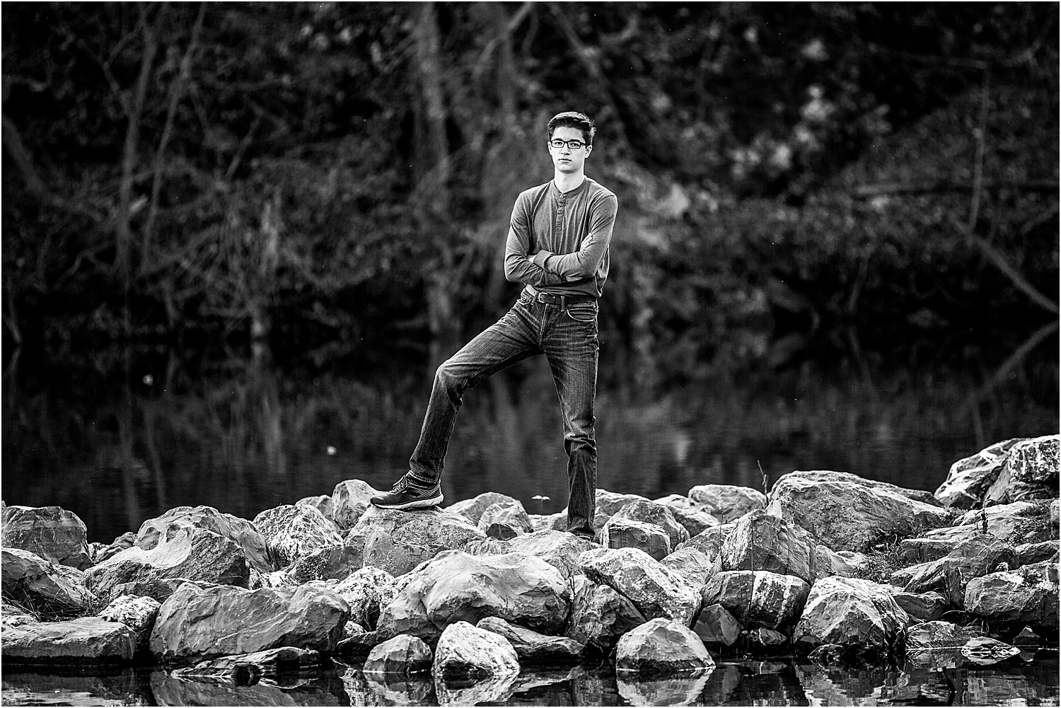 Black and white senior photo of boy standing near river