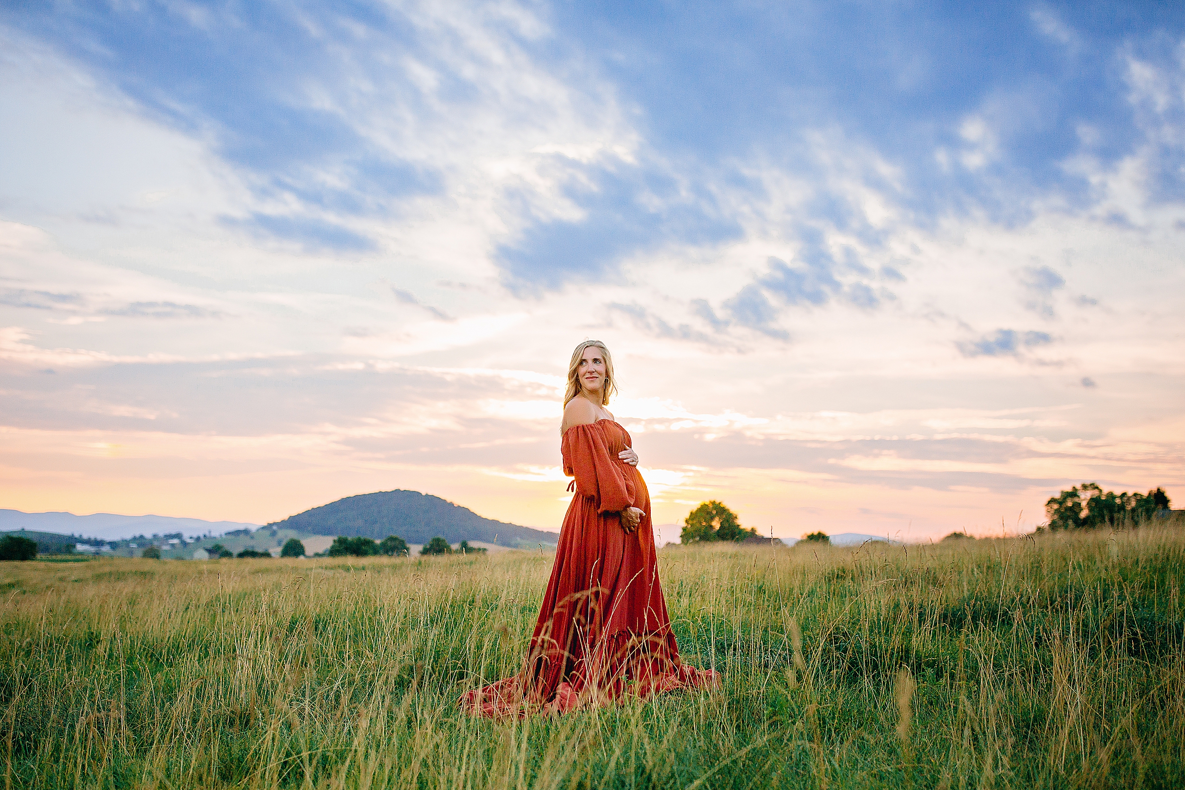 Pregnant woman in a field wearing a red dress at sunset