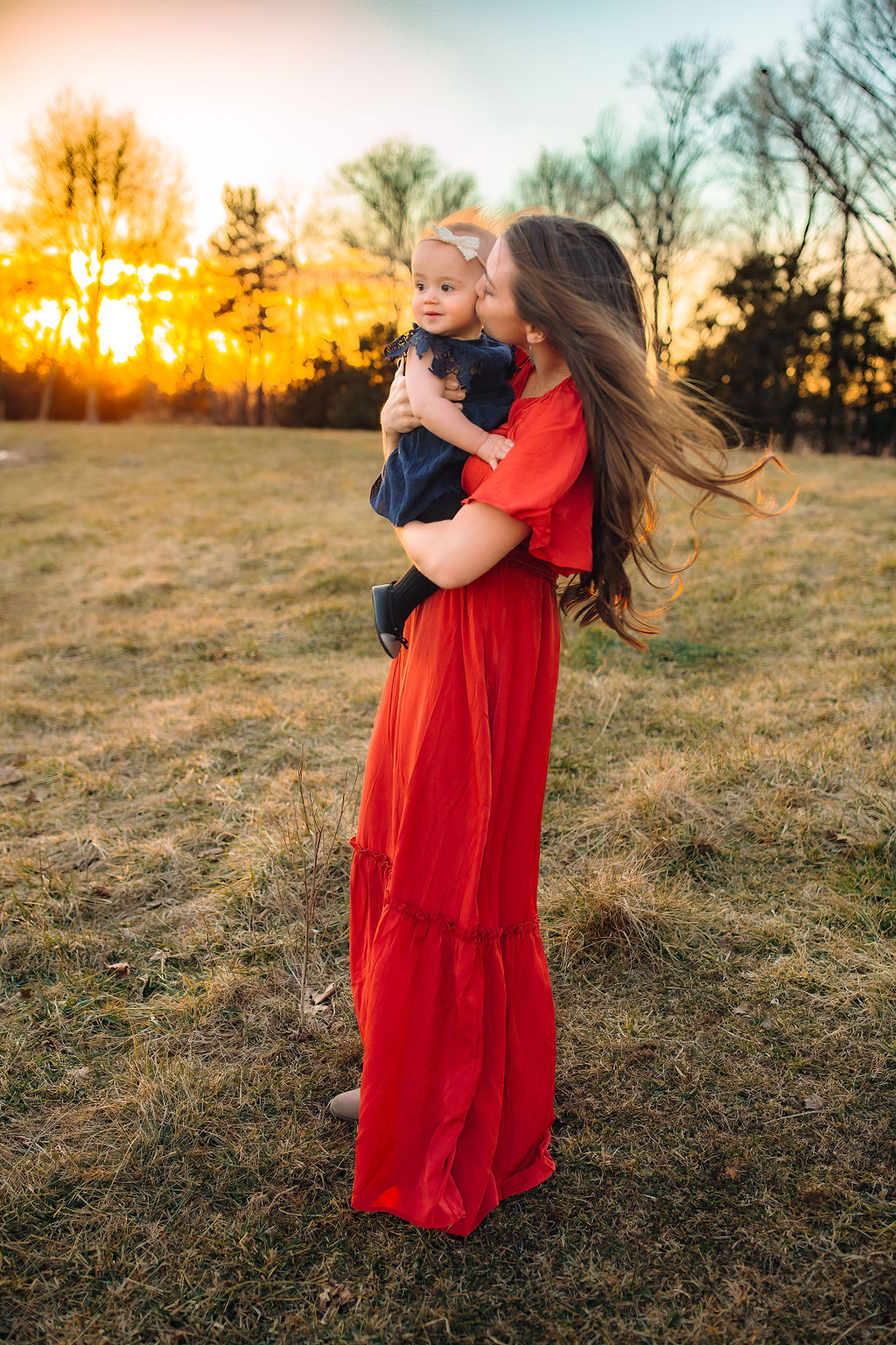 mom in red dress holds toddler in a field with a blue dress and bow EMU Musikgarten