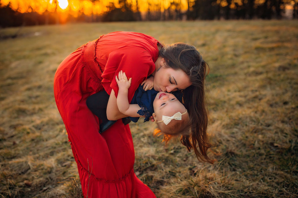 mom in red dress holds toddler updside down while kissing her