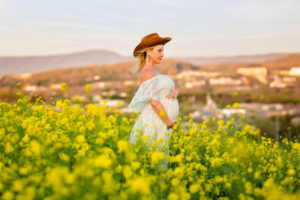 woman wearing a leather hat and white lace maternity gown stands in a field of wildflowers Sentara rmh labor and delivery