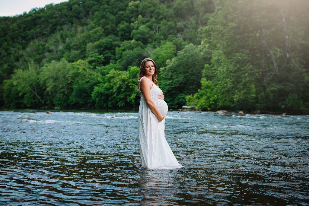 mom to be wearing white maternity gown stands in the river Shenandoah Womens health