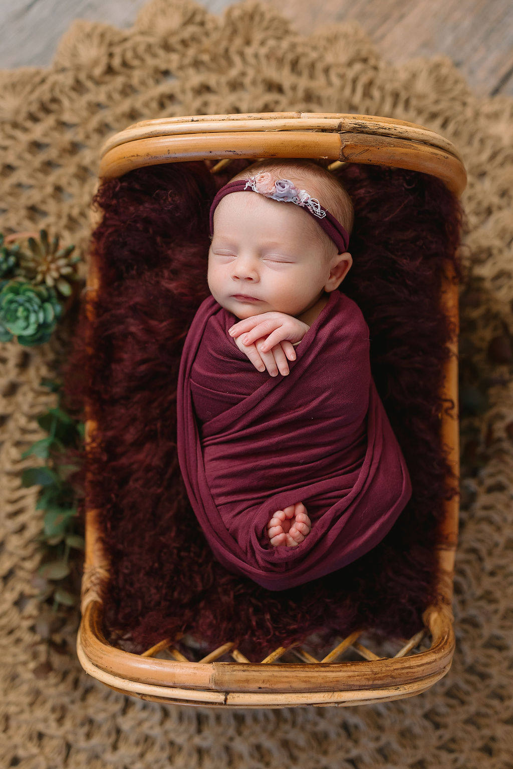 newborn sleeps while swaddled in purple in a wicker bed baby boutique charlottesville va