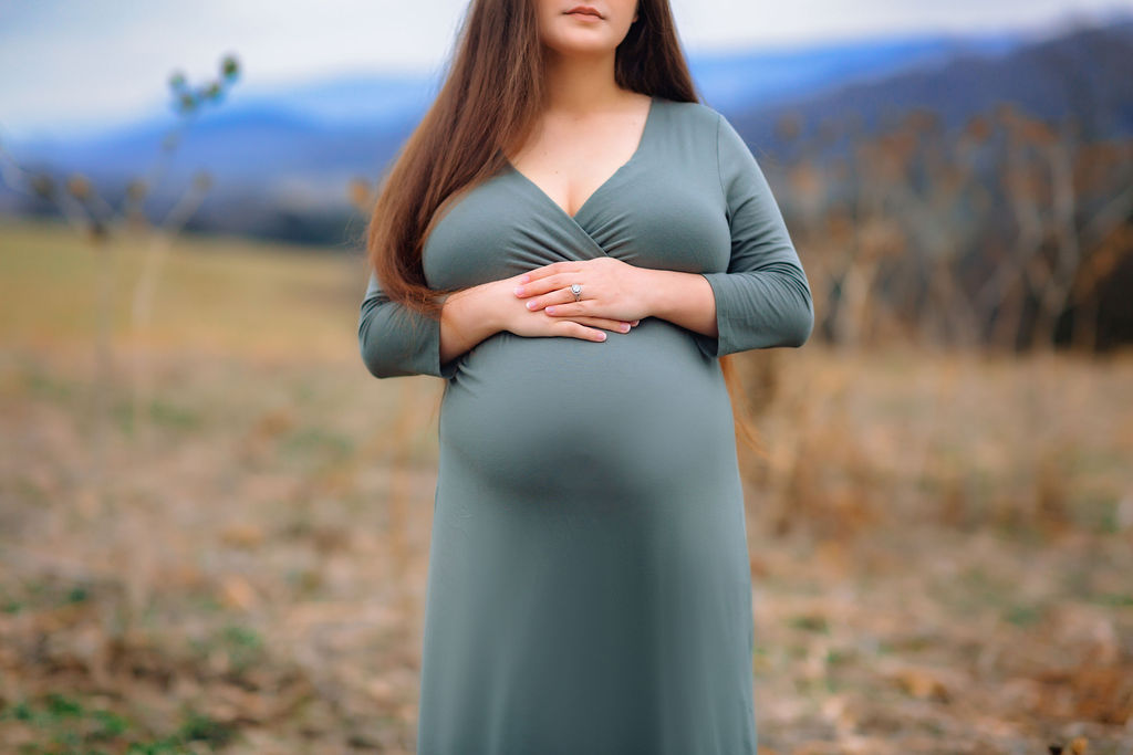 Pregnant mother to be stands in a field with hands placed over bump birth centre charlottesville