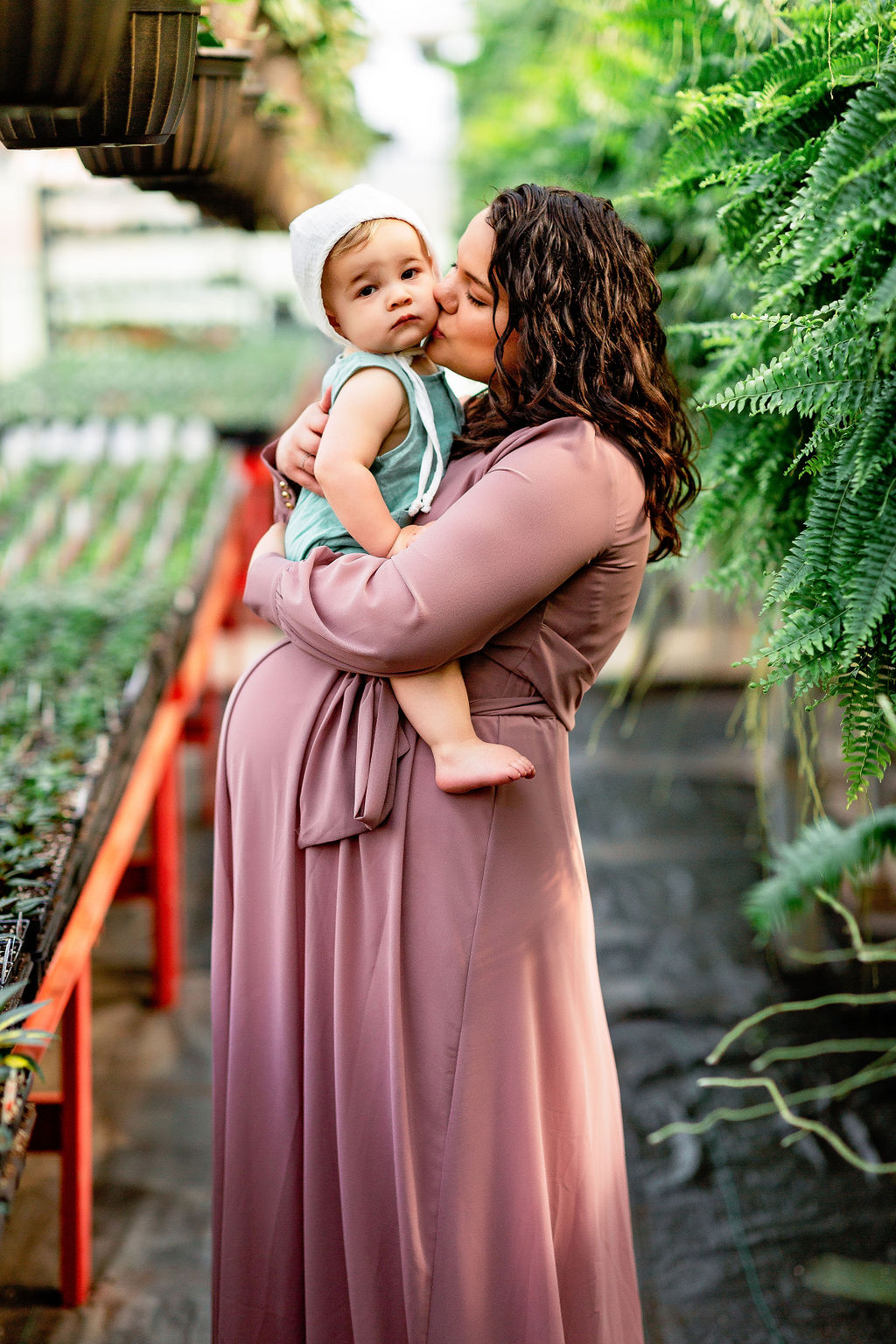 Pregnant mother kisses her toddler in a plant market birthing cottage