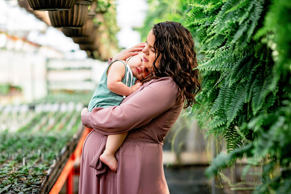 pregnant mother holds her older child in a plant market wearing a purple maternity dress birthing cottage