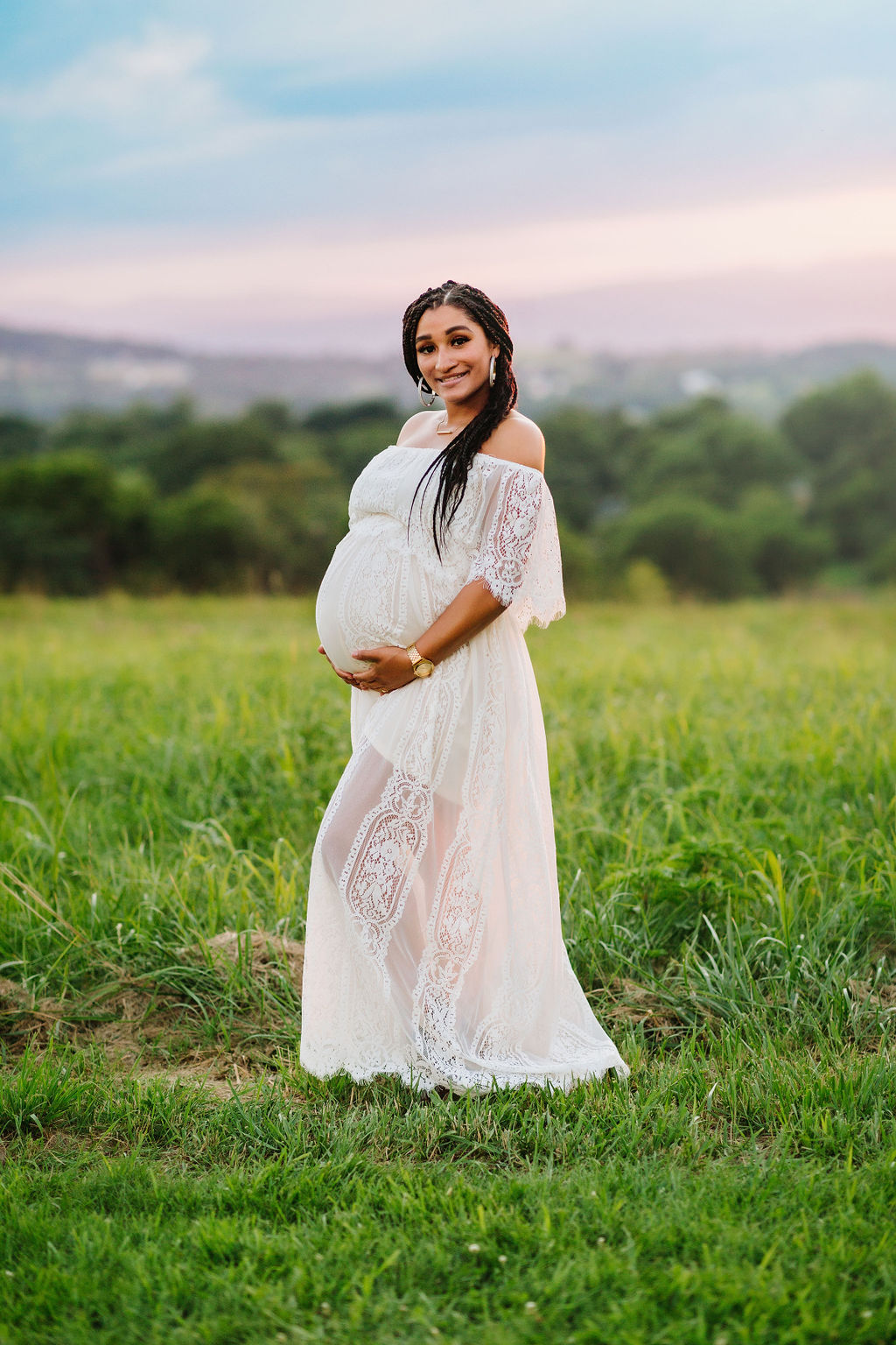 Mother to be holds her bump while wearing a white lace maternity drress