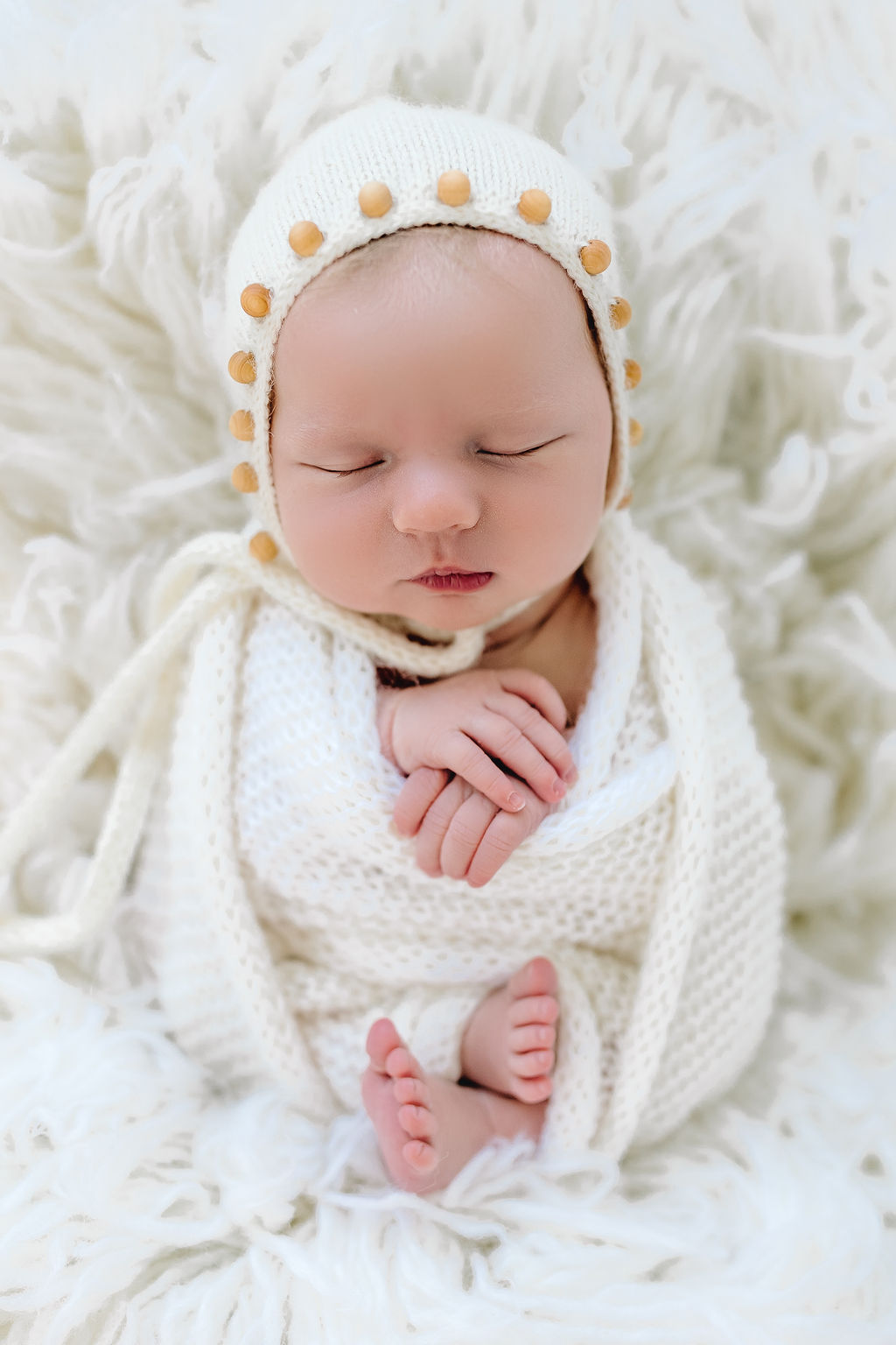 newborn swaddled in a knit blanket and hat sleeps on a fur blanket