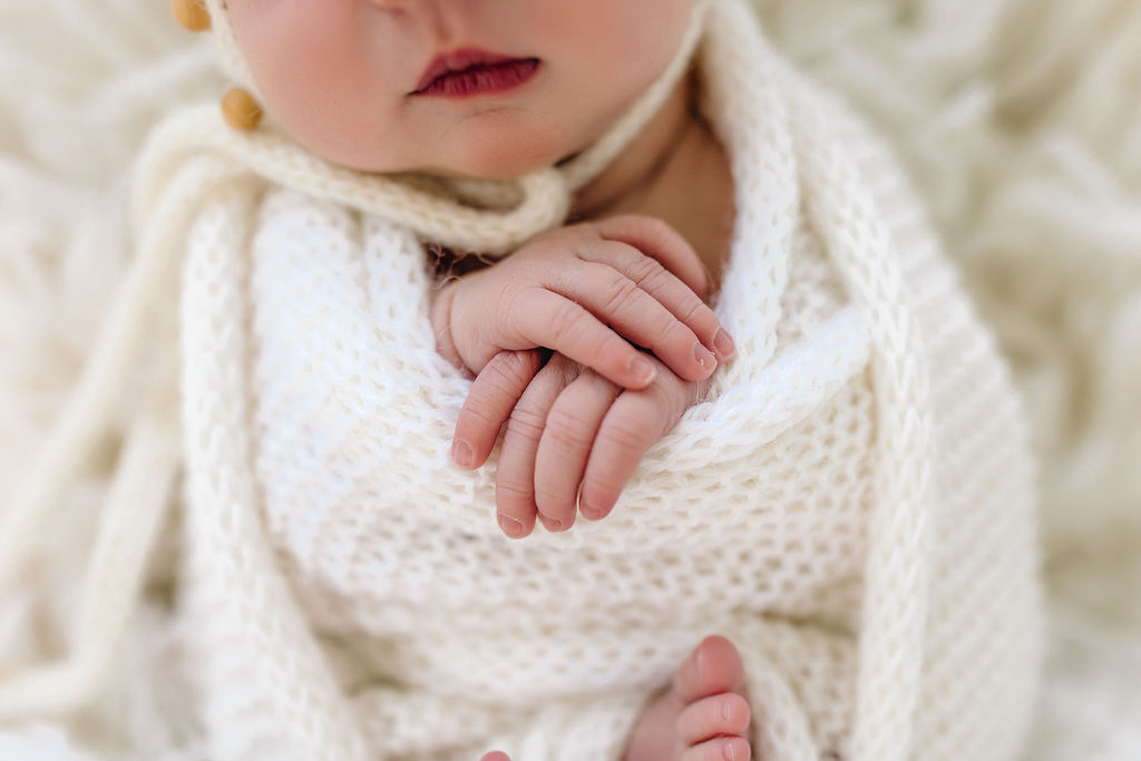 newborn's hands are crossed while sleeping in a knit swaddle green bean baby boutique