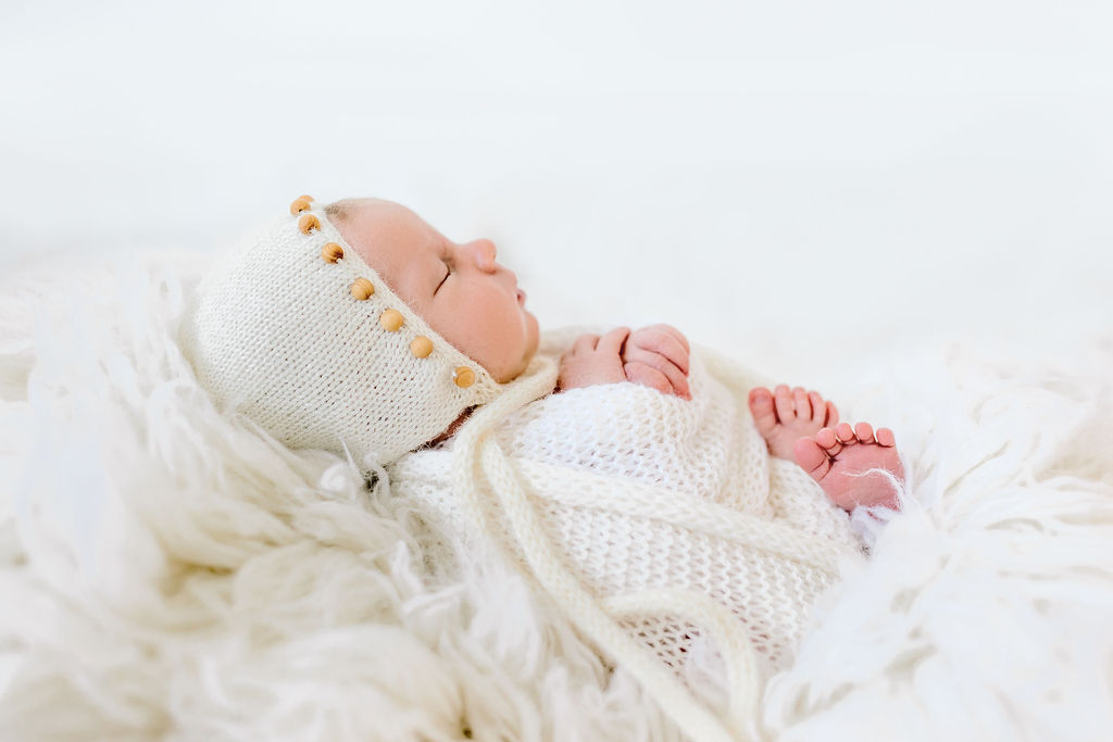 newborn sleeps in a knit outfit on a bed of fur in a studio green bean baby boutique