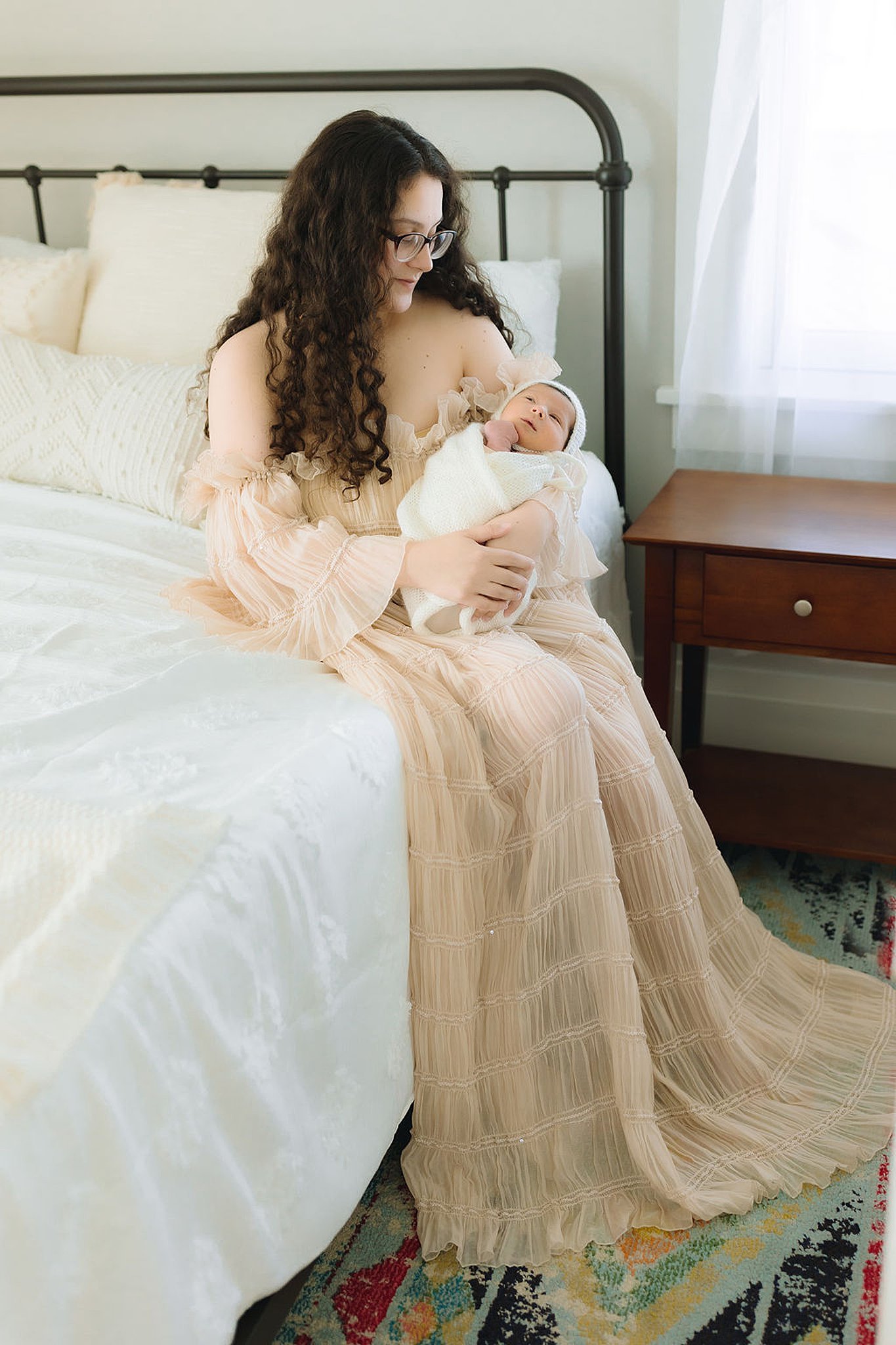 Mother cradles her swaddled newborn sitting on an iron frame bed lactation consultant charlottesville va