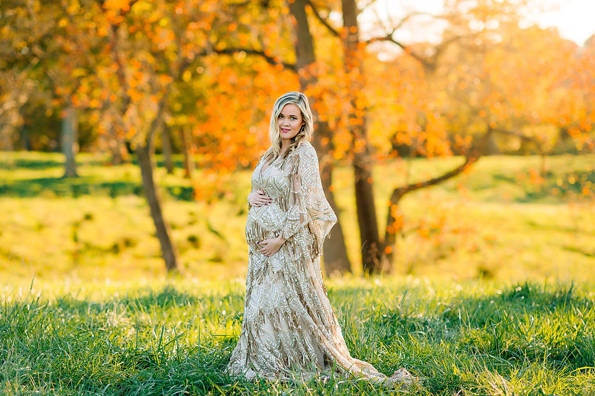 Mom to be wearing a patterned and beaded maternity gown holds her bump in a field midwives charlottesville