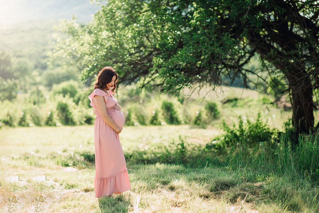 Mother to be looks down at her bump in a grassy field
