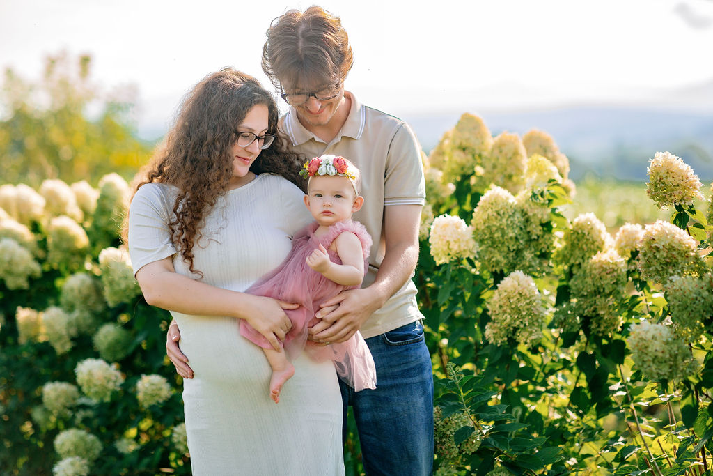mom and dad hold their toddler daughter in a flower garden