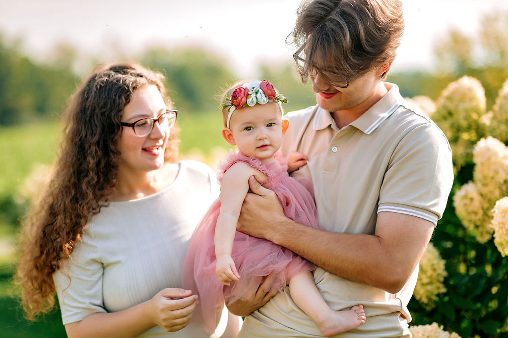 Dad holds his toddler daughter wearing a pink dress and flower headband in a flower garden