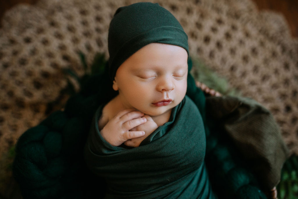 Newborn baby sleeps swaddled and propped up in a green swaddle and matching hat