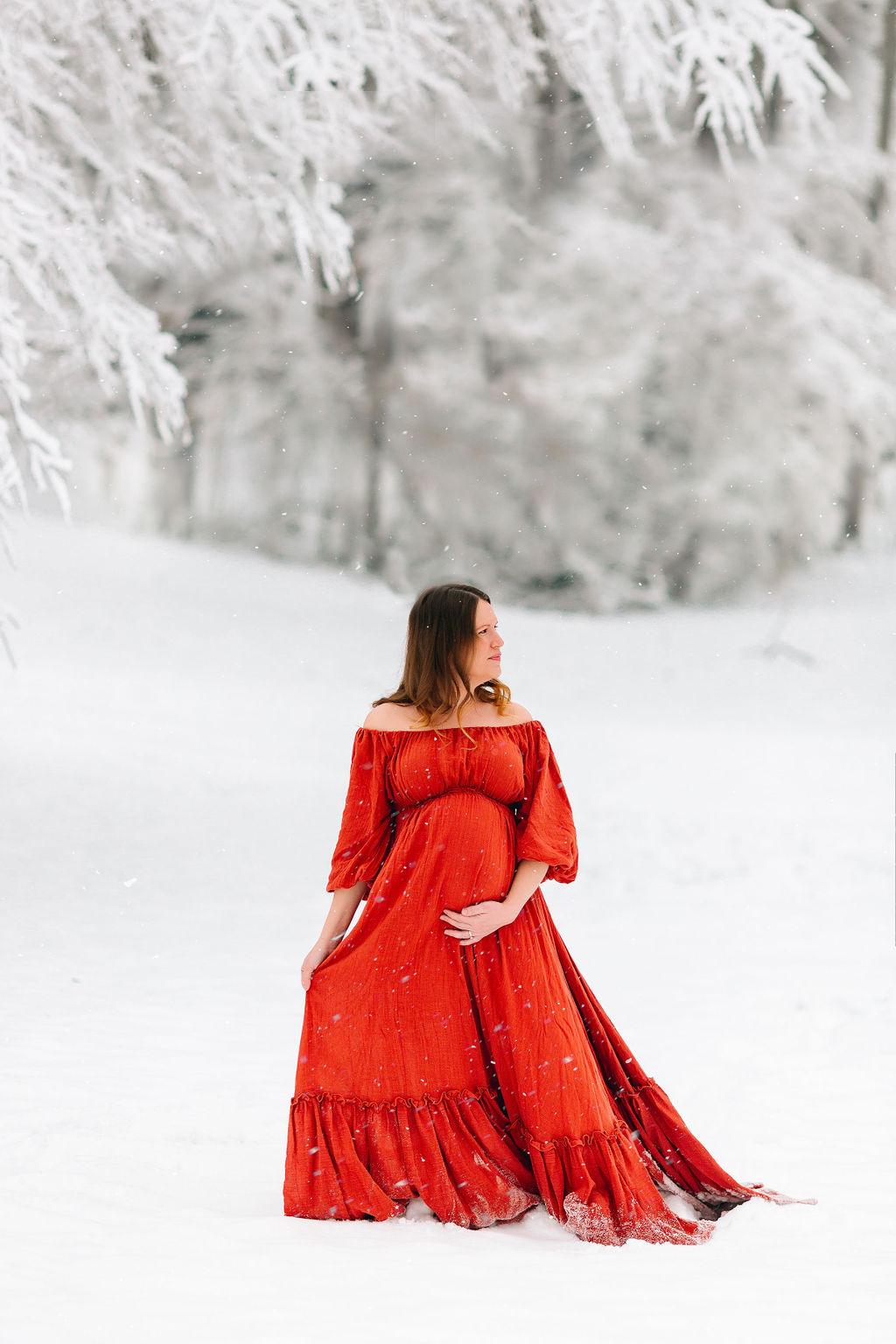 A mother to be stands out in fresh snow in a red maternity gown premier birth center
