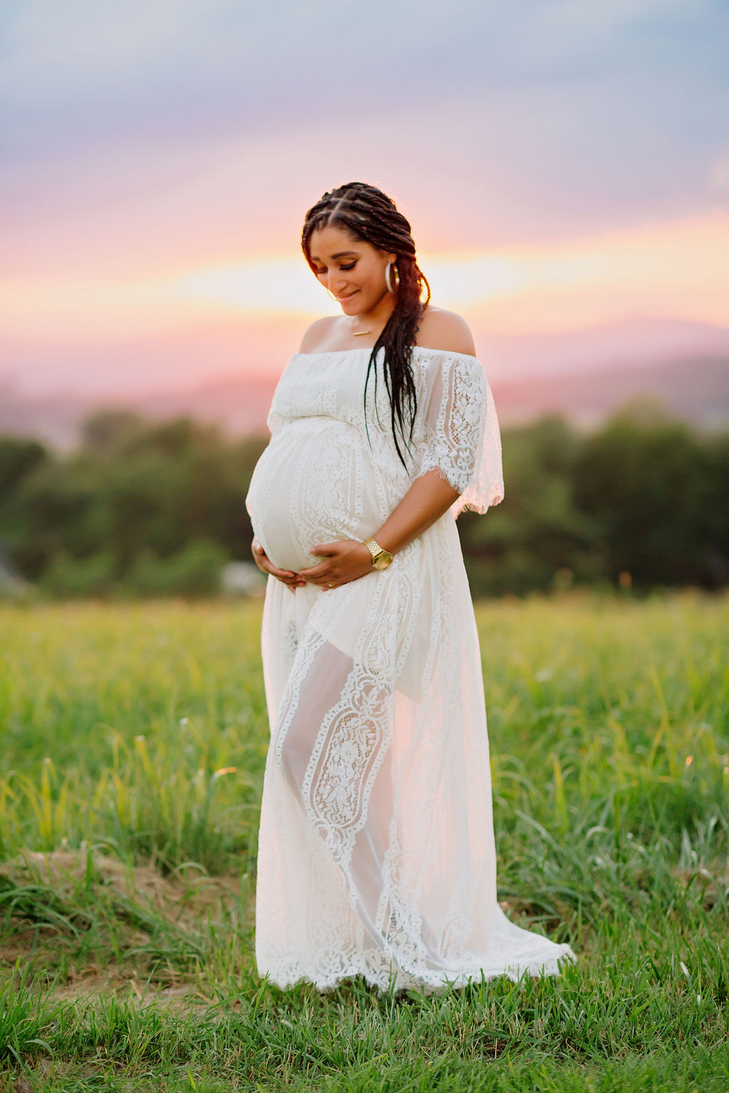 Mother to be stands in a grassy field in front of a vibrant sunset prenatal massage harrisonburg va