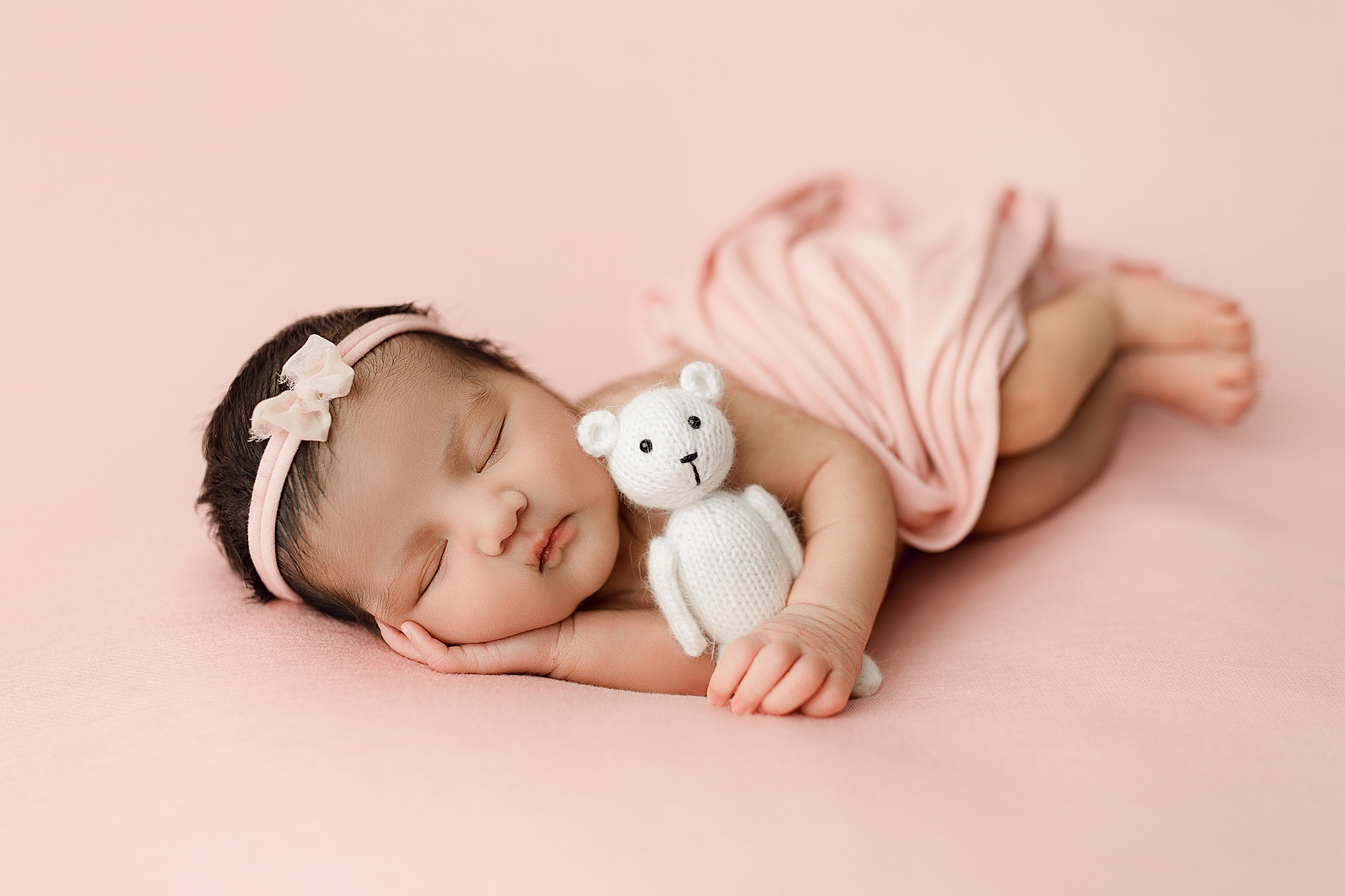 Newborn baby girl on pink fabric holding white bear