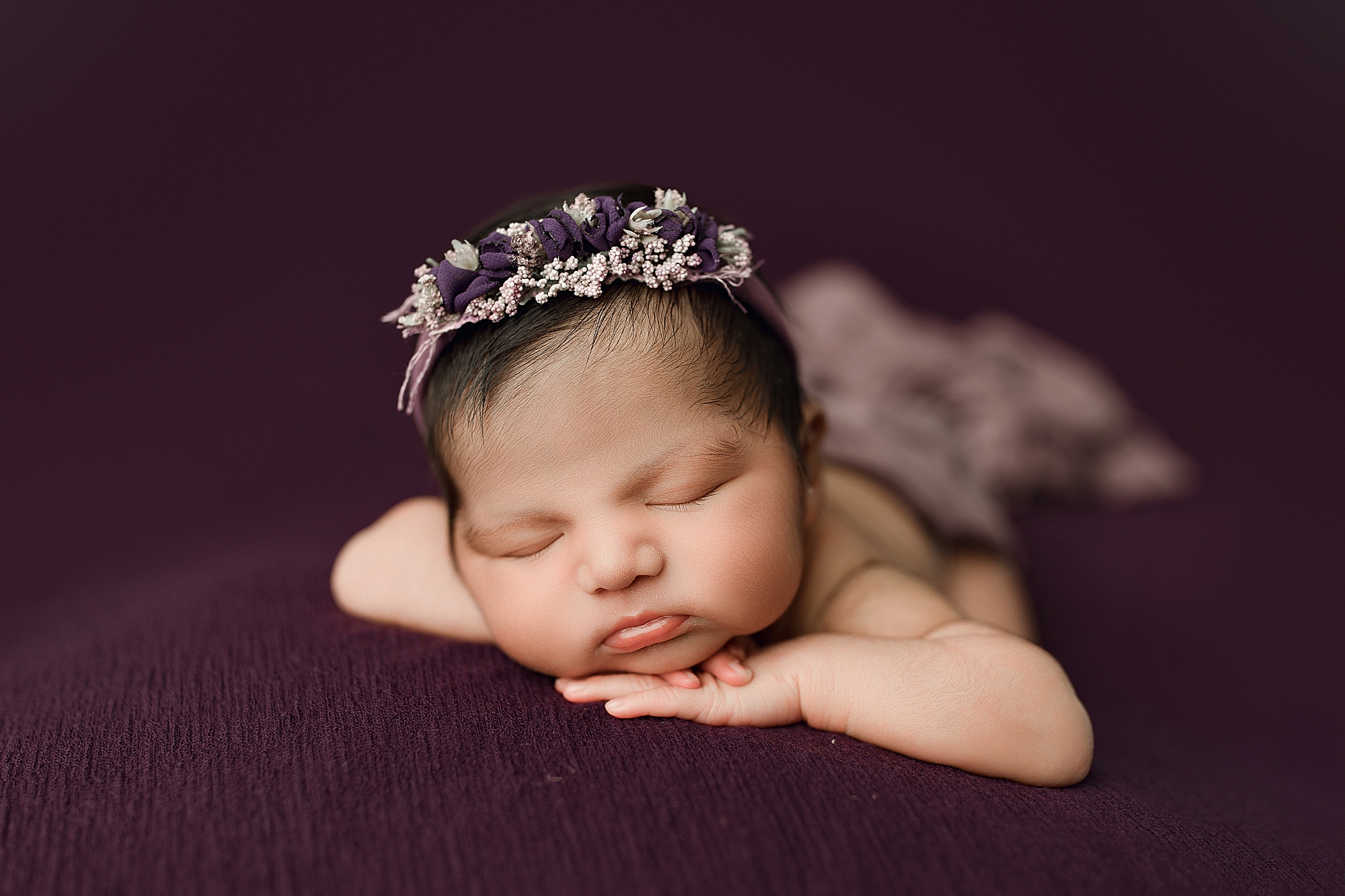 Newborn baby girl on purple fabric with flower crown