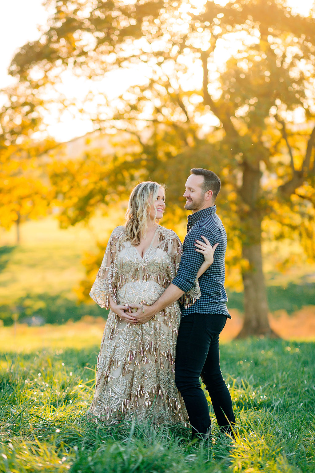 A mother to be stands in a grassy field in an ornate maternity gown with her partner putting his hand on the bump obgyn front royal va