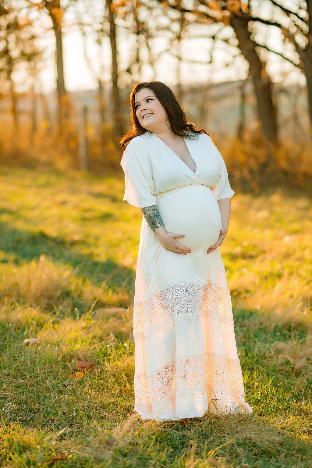 A mother to be looks over her shoulder while holding her bump in a white dress