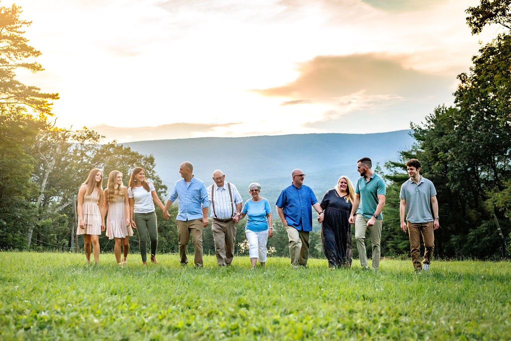 A large extended family walks through a green field up a hill holding hands and looking at each other activities at massanutten resort