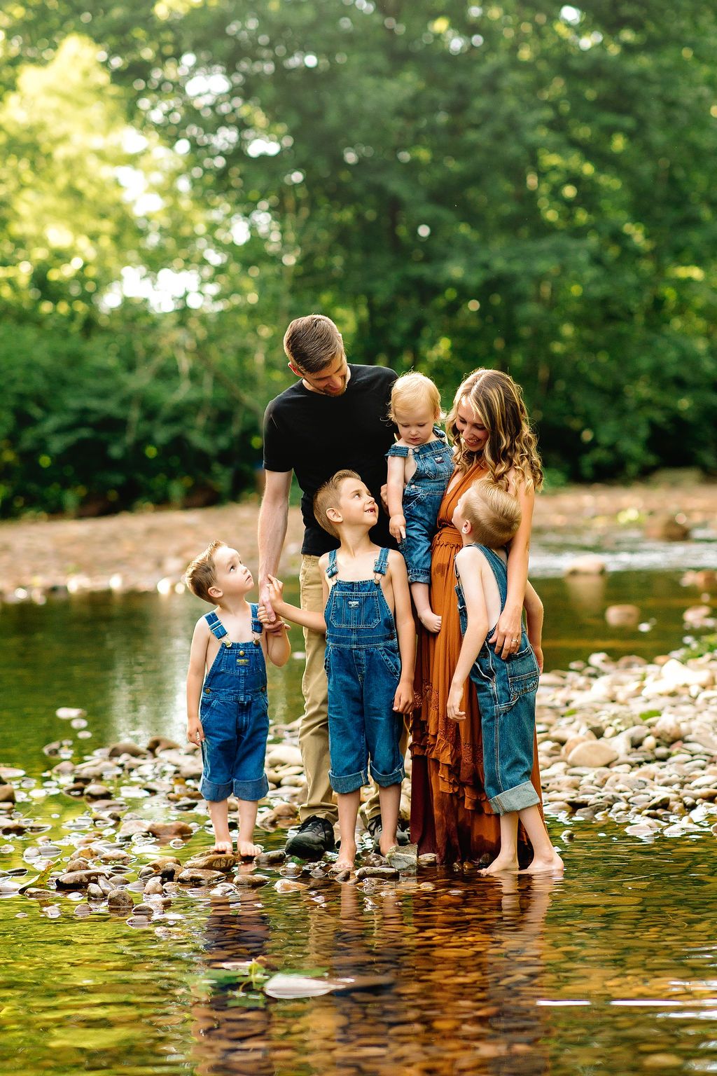 A family of six stands in the water of a rocky creek looking at each other