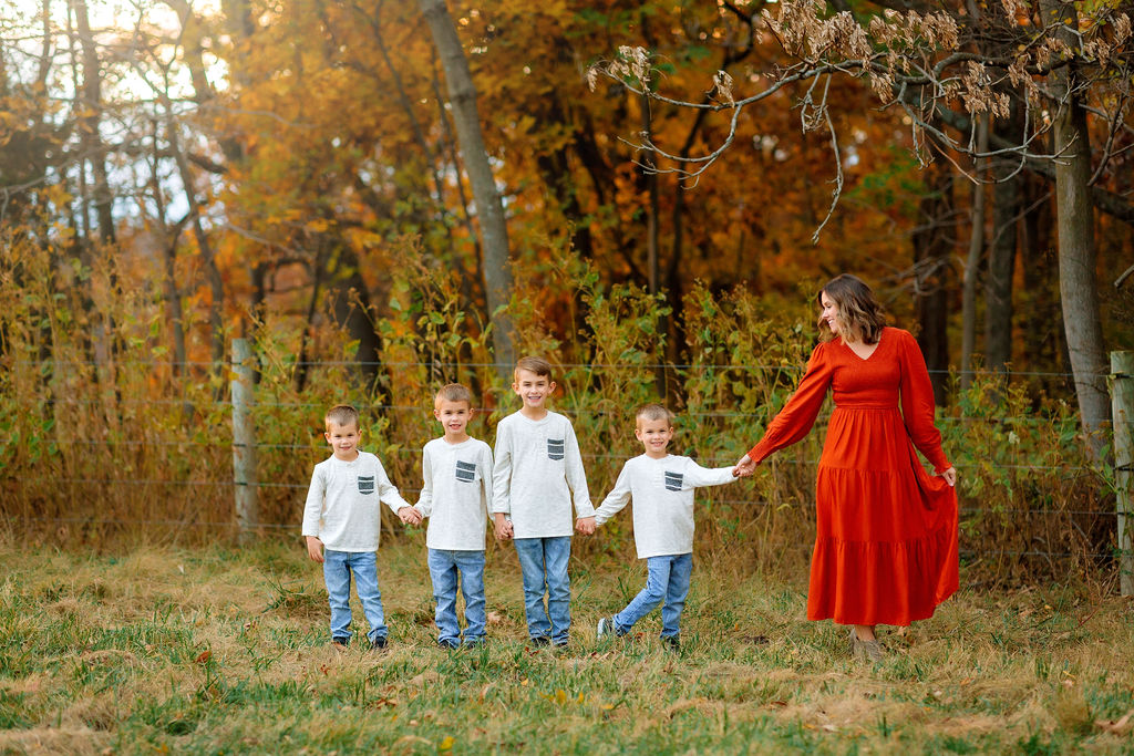 A mother in a red dress leads her four matching sons through a park while they all hold hands good shepard school harrisonburg va
