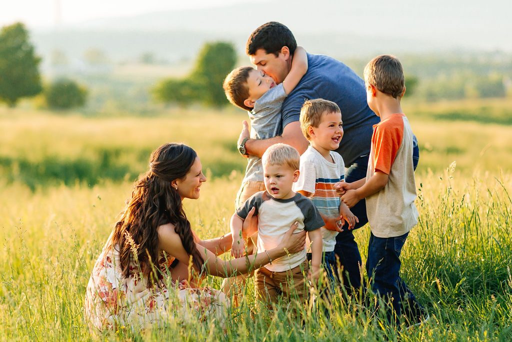 A mother and father play with their four boys in an open field with tall grass