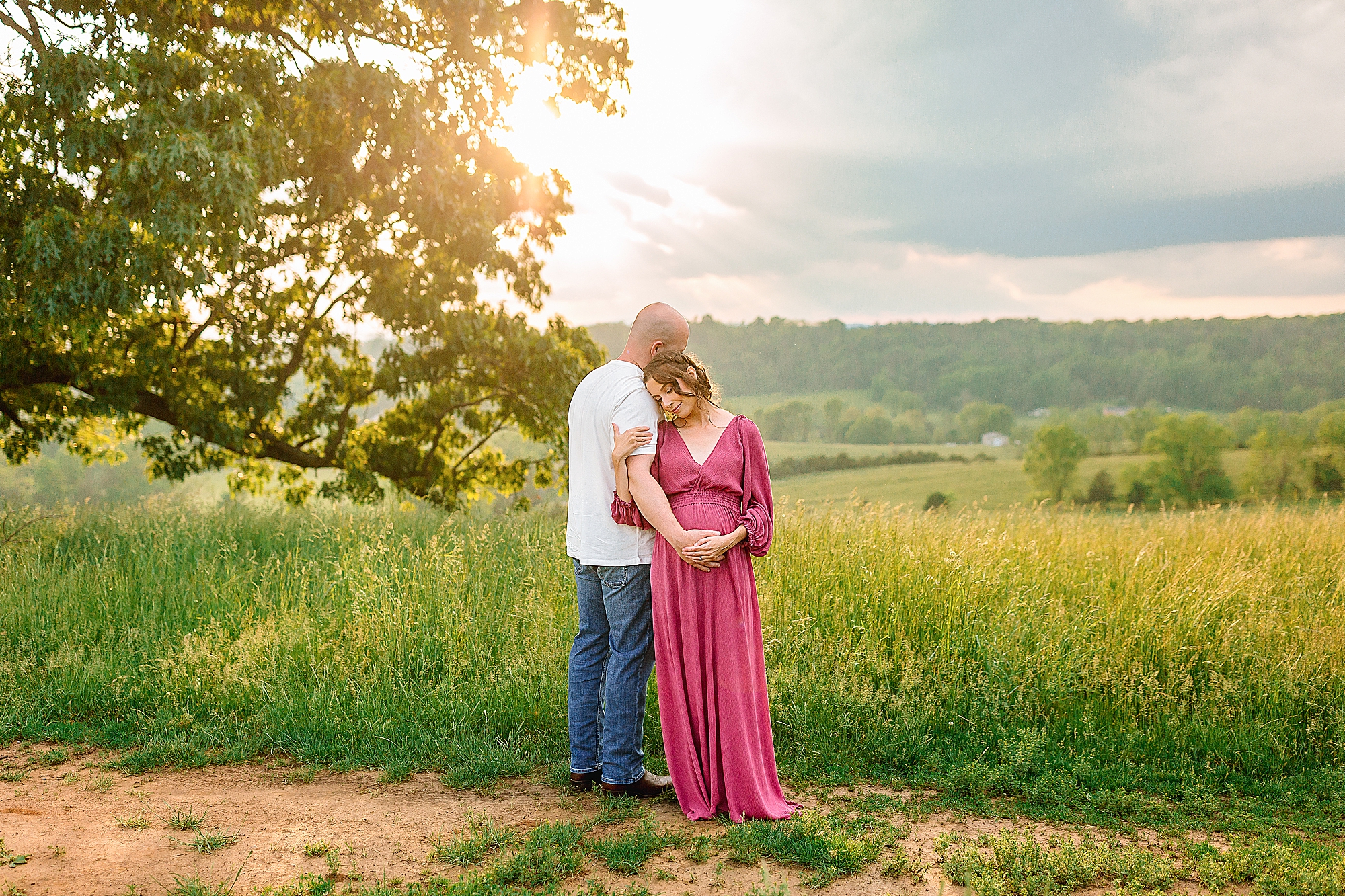 Husband and white posing with sunset in the background. Pregnant mom is wearing a pink dress.