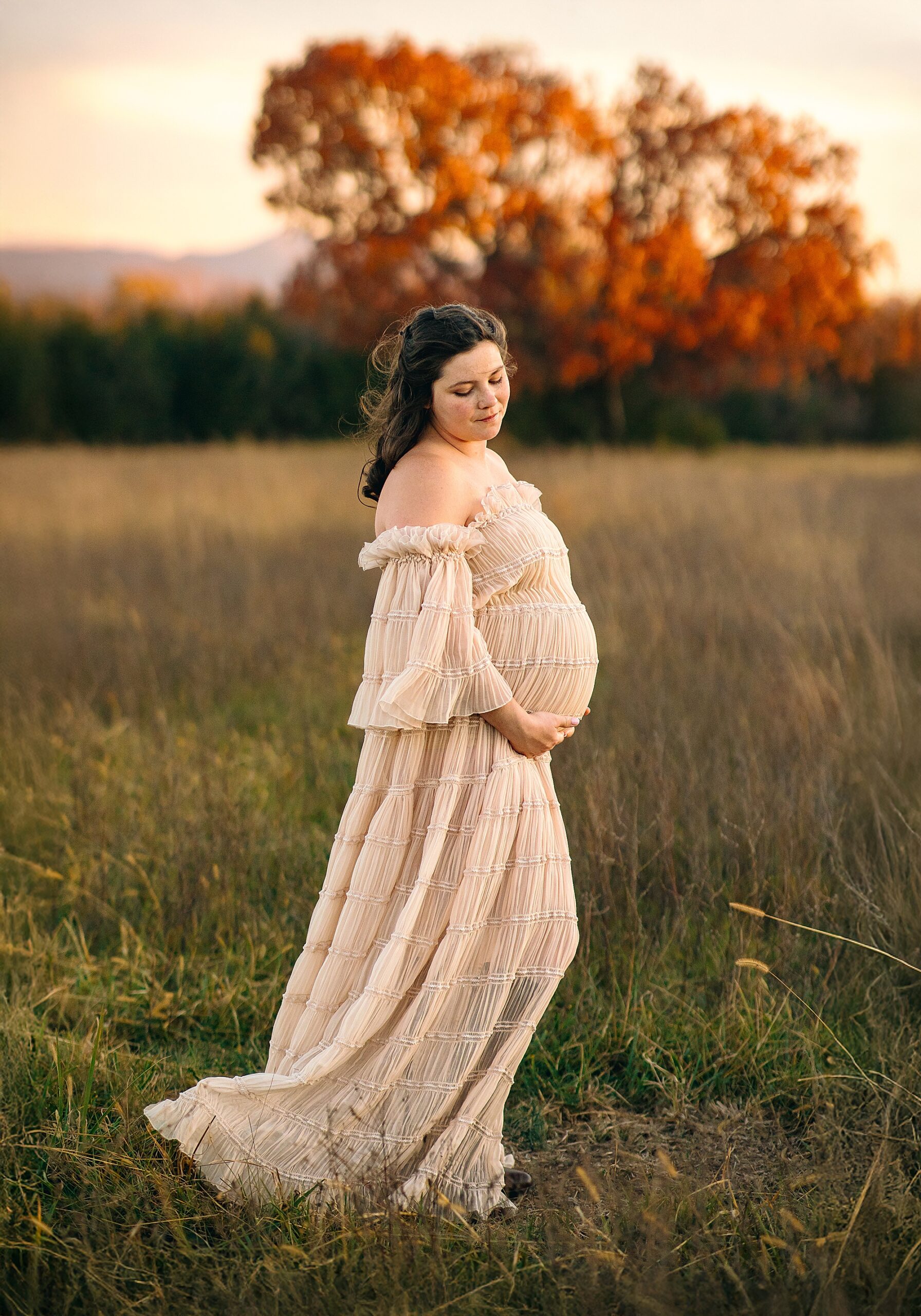 Maternity portraits in the fall in Harrisonburg. Woman in cream colored dress posing at sunset