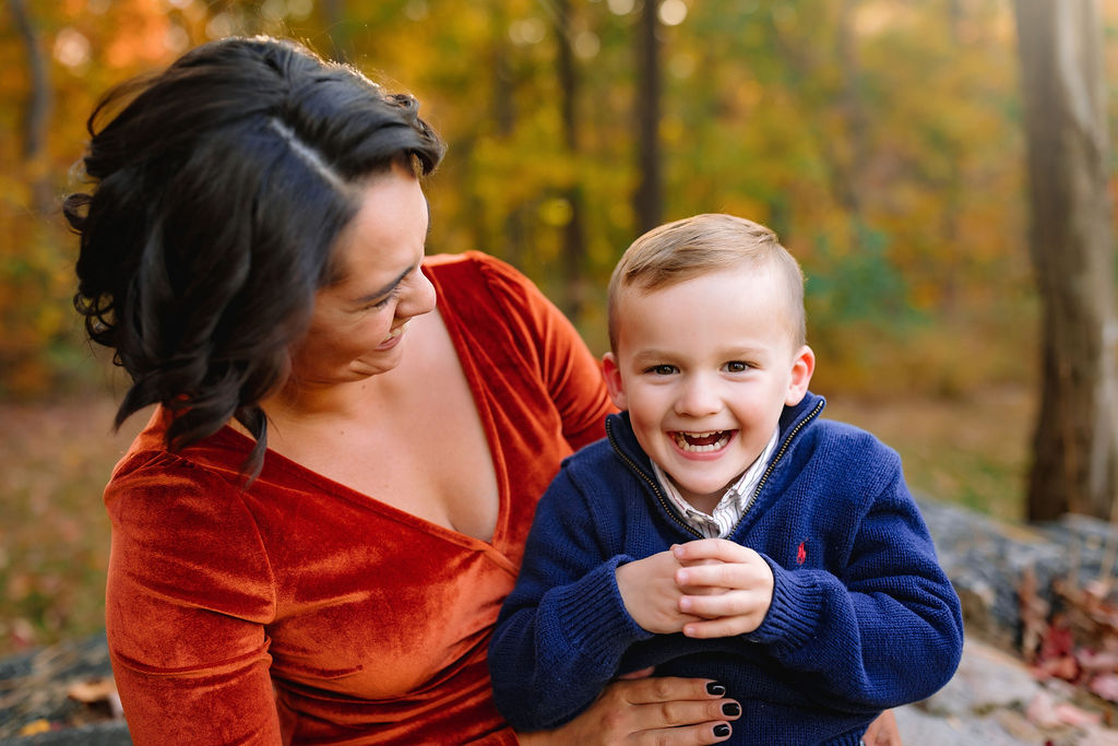 A mom in a red dress sits and plays with her young son in her lap in a forest harrisonburg pediatric dentistry
