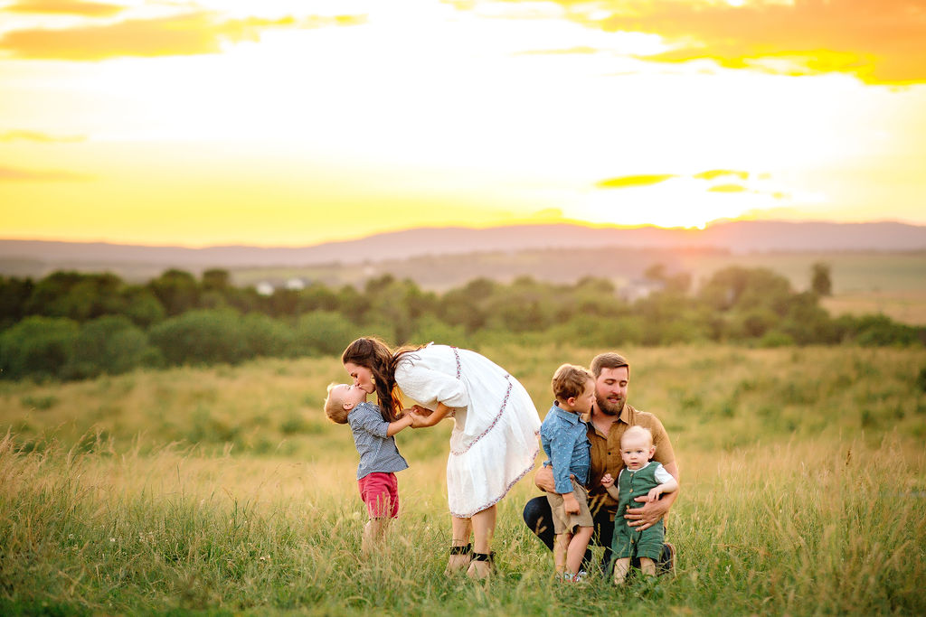 A family of five plays in the tall grass of a park at sunset
