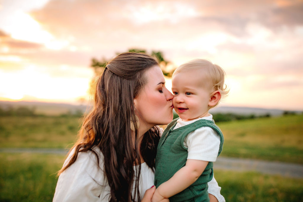 A mother kisses the cheek of her young toddler in herr arms in a park at sunset occupational therapy harrisonburg va
