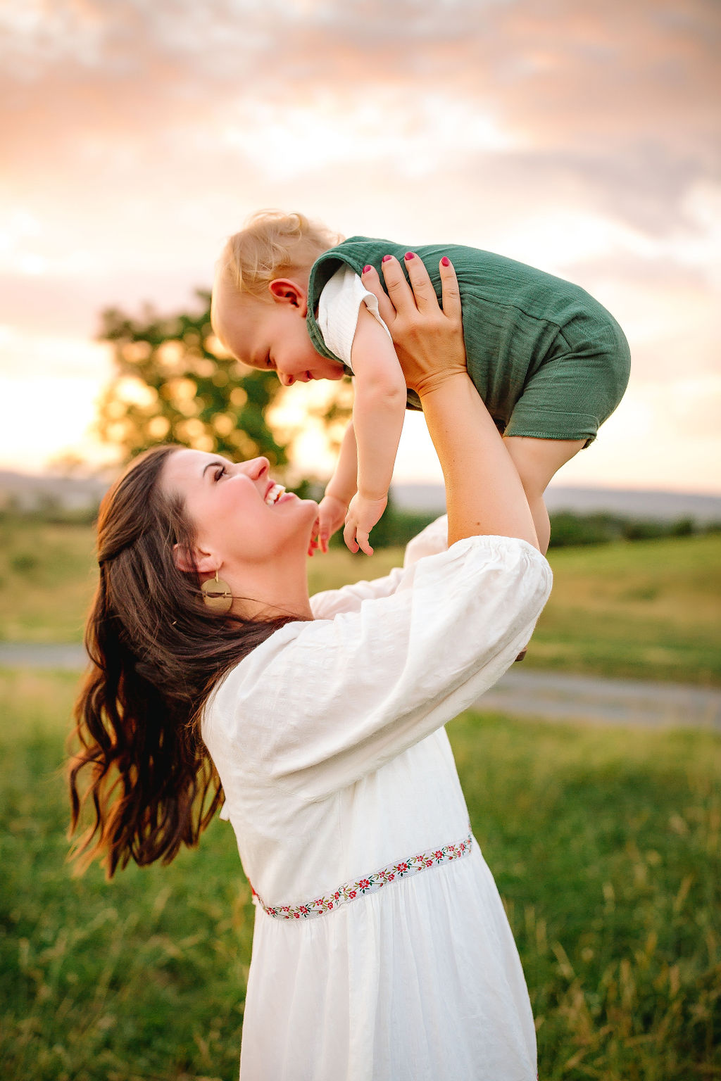 A mother in a white dress playing in a park at sunset by lifting her toddler above her head occupational therapy harrisonburg va