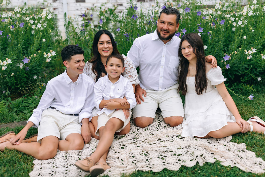 A family of five all in white sit on a lace blanket in a flower garden resorts near harrisonburg va