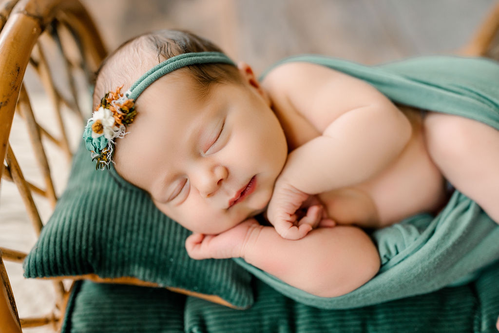 A newborn baby sleeps on a small bed with green blankets and pillows uva pediatrics