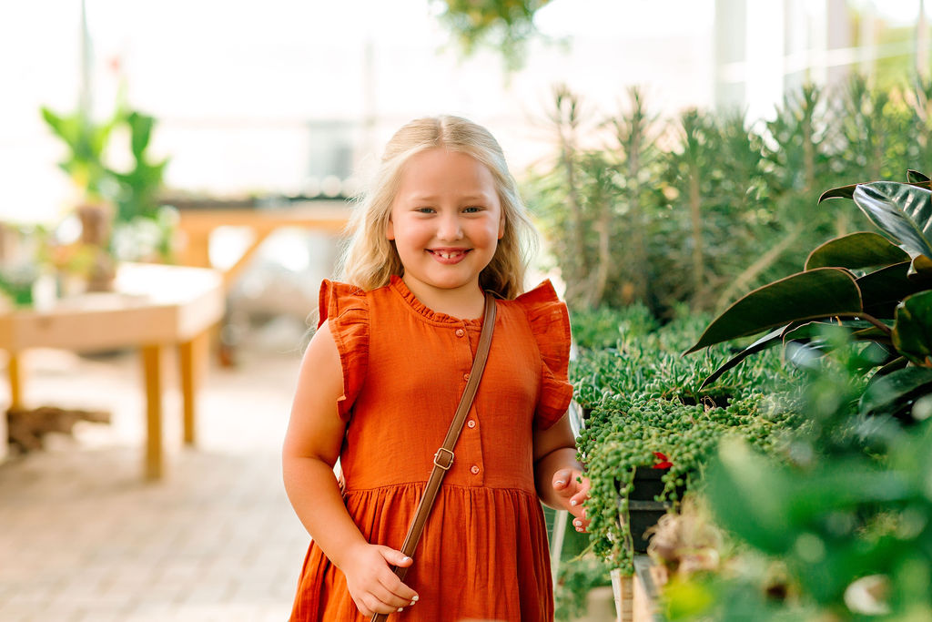 A young girl in a red dress walks through a greenhouse filled with plants winchester pediatric dentist