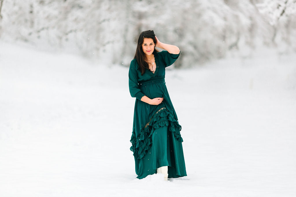 A mother to be in a teal maternity dress walks through snow while holding her bump women in motion