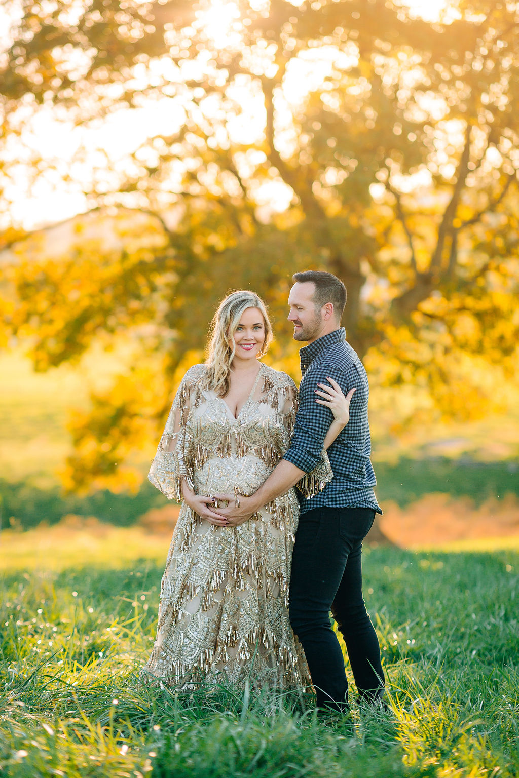 A husband hugs onto his pregnant wife while standing in a field at sunset Charlottesville ivf