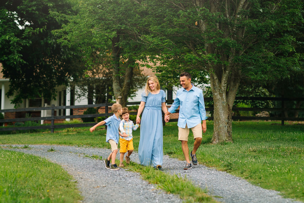 A mother and father wearing blue walk down a gravel road while holding hands with their two young sons charlottesville preschools