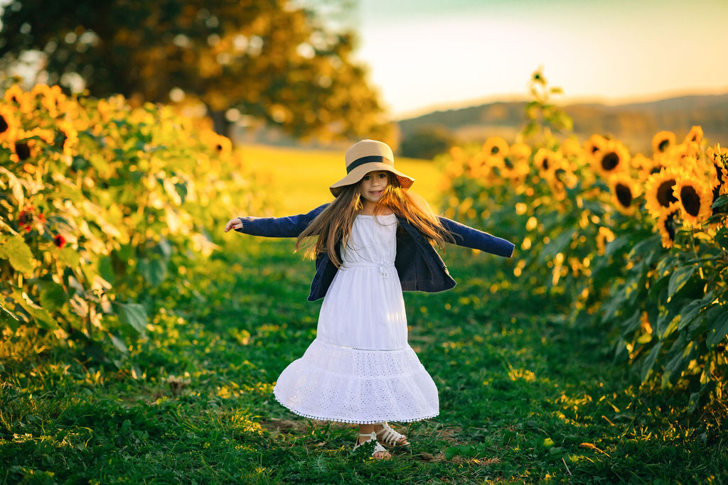 A young girl in a long white dress dances in a path in a field of sunflowers inmotion school of dance