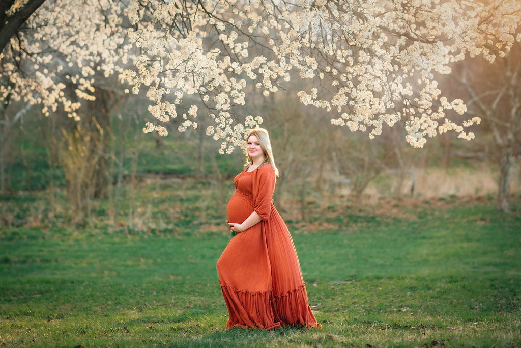 A mother to be walks through a grassy field at sunset in a red maternity dress