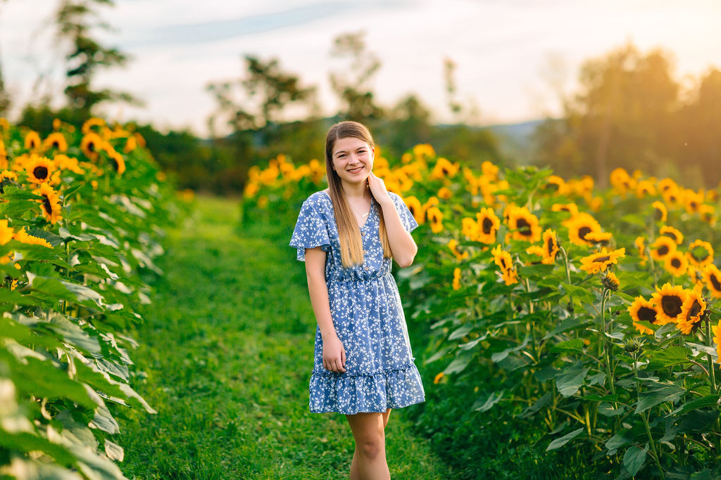 A teenage girl walks through a sunflower farm while wearing a blue dress
