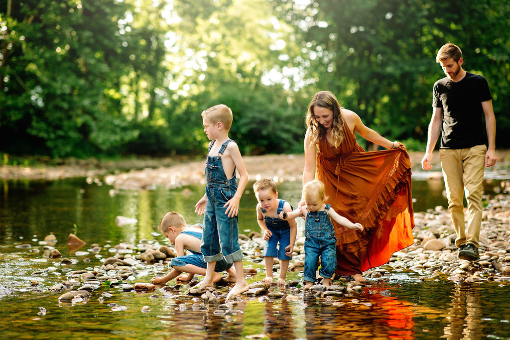 Four brothers in denim overalls play in a stream with mom and dad behind them swim lessons charlottesville va