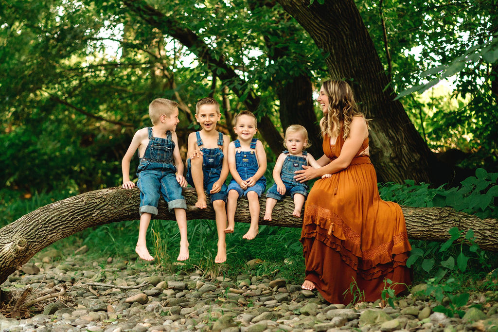 Four brothers sit on a tree branch wearing denim overalls with their mother in an orange dress swim lessons charlottesville va