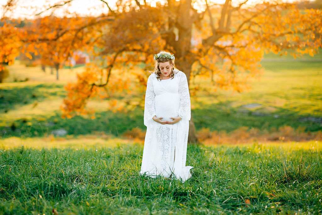 A mother to be gazes down at her bump in a white maternity gown