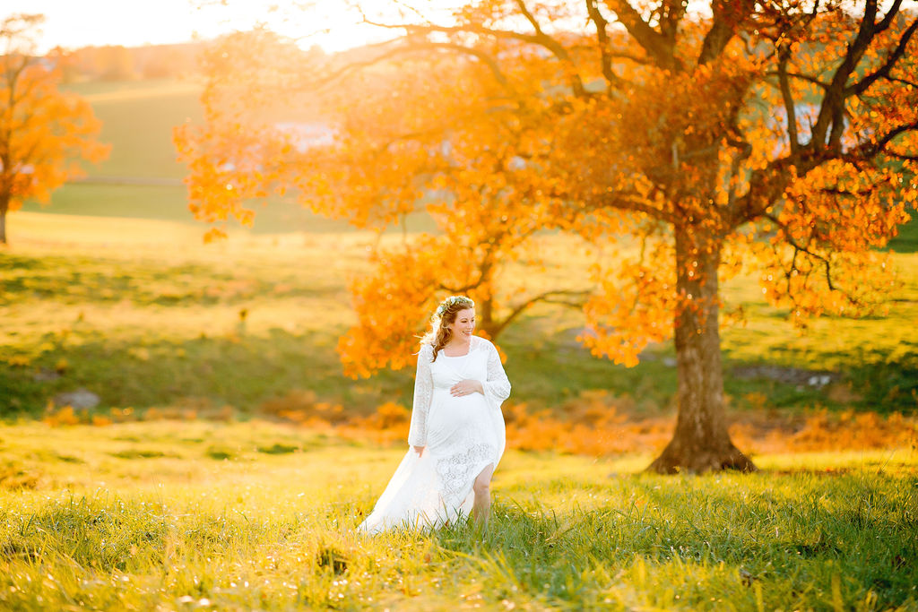 A mother to be in a white maternity gown walks through a field at sunset uva maternal fetal medicine