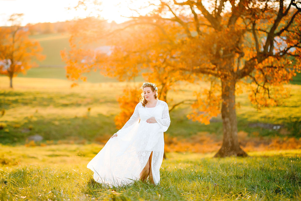 A mother to be walks through a field of green grass in a white maternity gown uva maternal fetal medicine